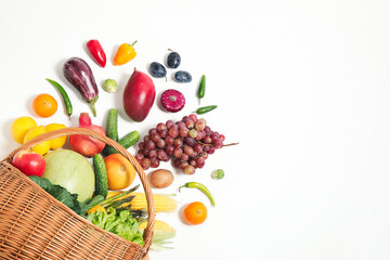 Basket with assortment of fresh organic fruits and vegetables on white background, top view