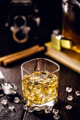 whiskey with ice on a wooden table, with decorative objects in the background, cigar, lighter and book.