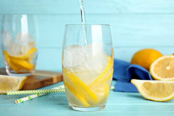 Pouring soda water into glass with lemon slices and ice cubes at light blue wooden table