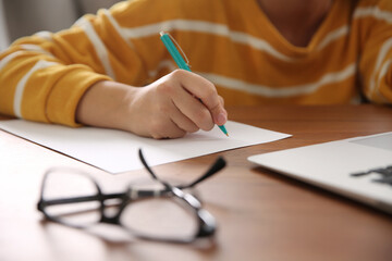 Woman writing letter at wooden table indoors, closeup