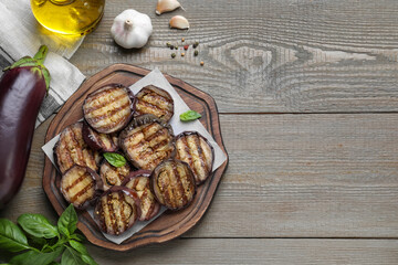 Delicious grilled eggplant slices served on wooden table, flat lay. Space for text