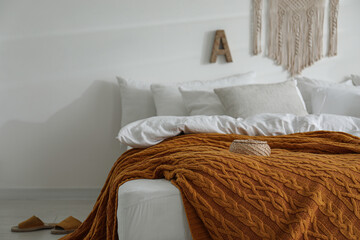 Warm orange knitted plaid on bed indoors