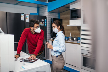 Obraz premium Young man talking with saleswoman in tech store. They are both with face protective masks. Pandemia, Covid-19 concept.
