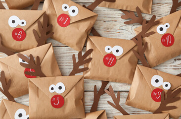 Set of gifts in envelopes with deer faces on white wooden table, flat lay. Christmas advent calendar