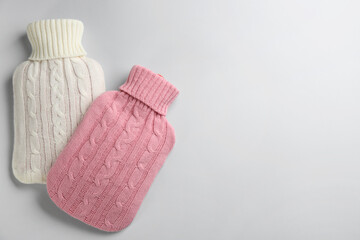 Hot water bottles with knitted covers on light background, flat lay. Space for text