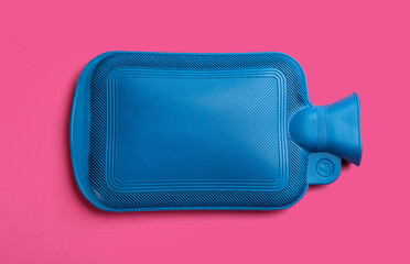 Blue rubber hot water bottle on pink background, top view