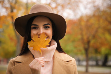 Young woman in stylish clothes holding yellow leaf outdoors, space for text. Autumn look - Powered by Adobe