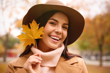 Young woman in stylish clothes holding yellow leaf outdoors. Autumn look