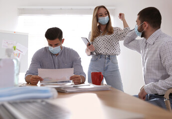 Coworkers with protective masks making elbow bump in office. Informal greeting during COVID-19 pandemic