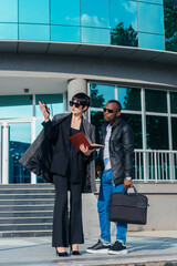 Full-length view of a business caucasian woman holding documents in front of the office building while talking with a black man