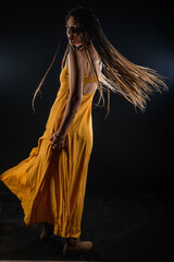 Mystic ancient queen goddess wearing a yellow dress on an isolated black studio background. Female feminist wearing braids and posing in a studio.