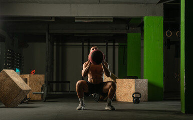 Fit man throwing medicine ball doing ball slam against gym floor or shoulder press exercise..