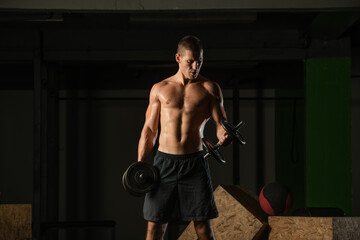 Fototapeta na wymiar Close up dark portrait of a shirtless young man exercising dumbbell alternate biceps curl