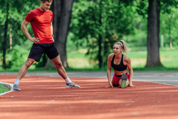 Young couple stretching before starting their morning jogging routine on a tartan track at the park.