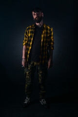 Full-length portrait of an attractive man with tattoos posing dressed in yellow and black checkered shirt on a black background