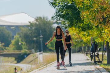 Two beautiful sportswomen roller skating in the park on a sunny day
