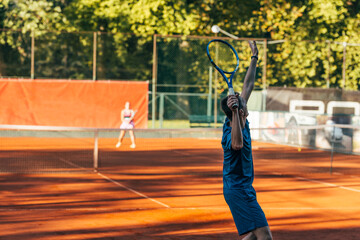 Fototapeta na wymiar Rearview of a tennis player ready to serve on a clay court wearing blue sportswear