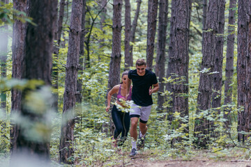 Fototapeta premium Young athletic couple is running outdoors in the wooded forest area