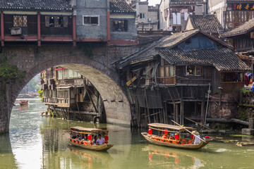 Fototapeta na wymiar FENGHUANG, CHINA - AUGUST 14, 2018: Boats passing under the arch of Hong bridge in Fenghuang Ancient Town, Hunan province, China