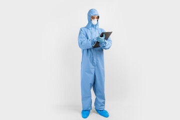 male doctor, dressed in a protective suit against coronavirus, glasses, mask and gloves, writes documents on an isolated white background. coronavirus, covid 19, medicine