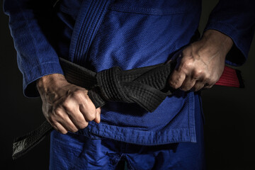 Close up on hand of unknown caucasian man holding brazilian jiu jitsu bjj black belt around his...