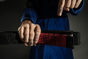 Close up on hand of unknown caucasian man holding brazilian jiu jitsu bjj black belt while wearing...