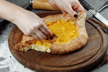 a young woman begins to eat fragrant khachapuri in ajarian with cheese on wooden support with a crisp crust