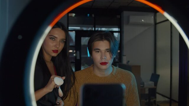 Makeup studio - young handsome man with bold red lipstick and his make up artist about to film a video