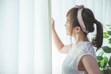 白いカーテンから差し込む朝日を浴びる若い女性
