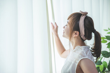 白いカーテンから差し込む朝日を浴びる若い女性
