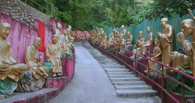 Tracking out (TUT) of buddha statues in rows. Ten Thousand Buddhas Monastery's main alley, Sha Tin, Hong Kong, China. Peaceful golden religious sculptures. High dynamic range footage in 4K.