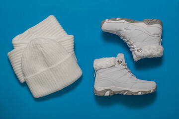 White winter women's shoes, scarf and hat on a blue background.