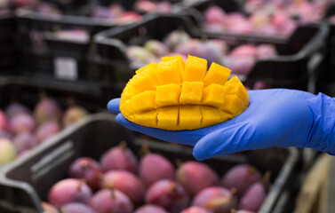 Fresh ripe sliced mango on hand in glove, blurred boxes with fruits on background