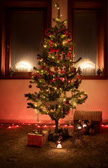 Christmas tree with decorations in a room. Candles and christmas present under the tree. Christmas lights in the windows. 