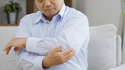 リビングで肘を撫でる中高年男性