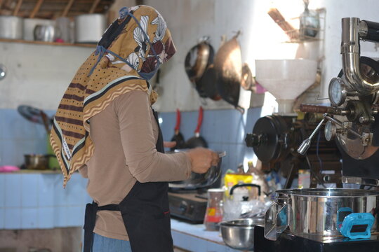 A female coffee roaster is roasting coffee beans using a roasting machine