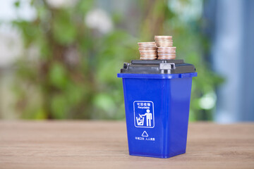 A model of a trash can with recyclable trash and a pile of dollar coins on its lid
