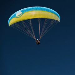 Paragliding in the sky. Yellow paraglider in dard blue sky. Bavaria. Germany. 