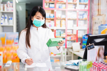 Cheerful positive chinese woman pharmacist keeps track of drugs in interior of pharmacy