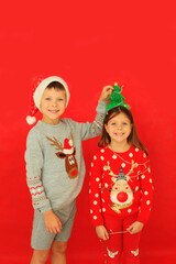 Boy and girl in New Year's sweaters on a red background. Two children in Christmas outfits