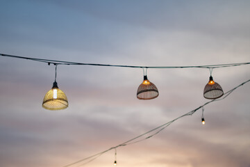 Blurred pastel colored sunset sky against string decorative light with bamboo fish trap lamp.