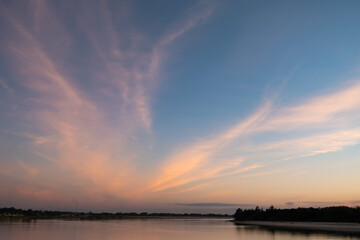 Sunset sky and Cirrus fibratus clouds over the riverbank of Mekong river. Blue and orange colors evening sky background.