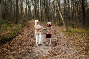 Fototapeta premium Caucasian children sisters walk together in the park in the forest, girlfriends children hold hands and hug for a walk, girly secrets, autumn walks in warm coats