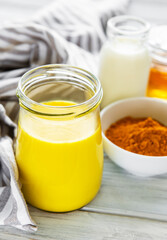 Yellow turmeric latte drink. Golden milk with cinnamon, turmeric, ginger  and honey over white wooden background.