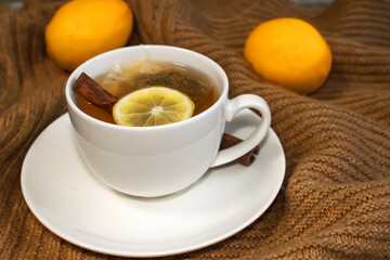 Close-up of a white Cup with tea lemon and cinnamon that stands on a warm yellow sweater on the background of blurred lemons.
