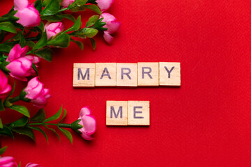 Wooden block lettering "marry me" on red textured background with bouquet of roses: wedding  background, top view