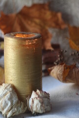 Fototapeta na wymiar Tall golden candle with dried flowers at the base and autumn background