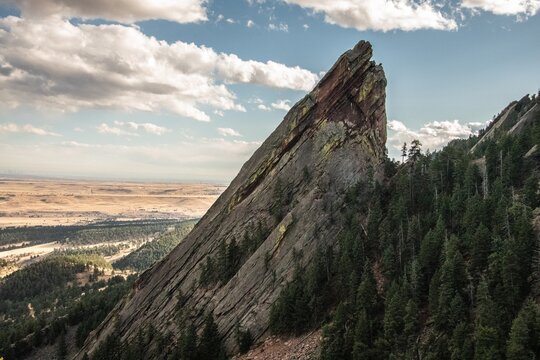 Flatiron in Boulder, Colorado. This view shows the rock face coming above the horizon with a blue sky with clouds and a city in the background