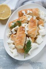 Filo mini rolls with feta cheese stuffing on a white oval plate, vertical shot on a white concrete surface, selective focus