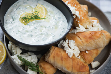 Close-up of greek phyllo rolls with feta cheese filling and a bowl of tzatziki dip sauce, selective focus